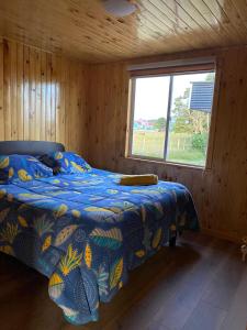 1 dormitorio con 1 cama con edredón azul y ventana en Cabañas El Viejo Roble, en Castro