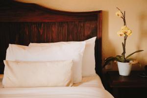 - un lit avec des oreillers blancs et un vase avec des fleurs sur une table dans l'établissement Docecuartos Hotel, à San Cristóbal de Las Casas