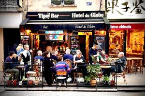 un grupo de personas sentadas en las mesas fuera de un restaurante en Hostel Du Globe, en París