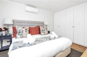 een witte slaapkamer met een groot bed met kussens bij Cosy New Home in Claremont in Kaapstad