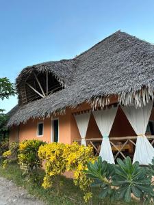 a house with a thatched roof and yellow flowers at SAMAKI VILLAGE in Watamu