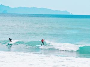 two people riding a wave on surfboards in the ocean at Aotearoa Surf Eco Pods in Te Arai