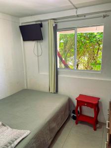 1 dormitorio con cama, ventana y mesa roja en Casa beira do mar en Florianópolis