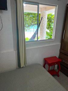 a bedroom with a bed and a window with a red stool at Casa beira do mar in Florianópolis