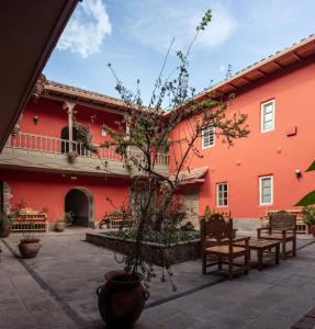 a red building with benches and a tree in the courtyard at Tambo del Arriero Hotel Boutique in Cusco