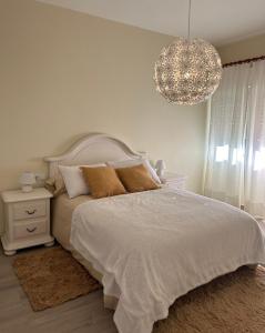 ein weißes Schlafzimmer mit einem Bett und einem Kronleuchter in der Unterkunft Acogedor Bajo en Meira in Moaña