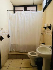 a bathroom with a white shower curtain and a toilet at Old Bells Hostel in Santa Ana