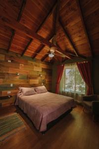 1 dormitorio con paredes de madera, 1 cama y ventana en Cabañas Los Maquis, en Pucón