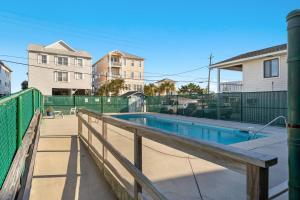 a swimming pool with a wooden rail and a fence at Portabella Paradise in Carolina Beach