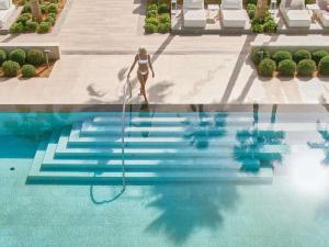 une femme en bikini saute dans une piscine dans l'établissement Grecotel LUX.ME White Palace​, à Adelianos Kampos