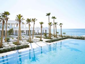a large swimming pool with palm trees and the ocean at Grecotel LUX.ME White Palace​ in Adelianos Kampos