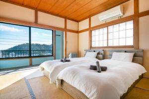 2 camas en una habitación con ventanas grandes en 湯河原「ゲストハウス城堀の家」, en Yugawara