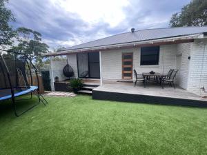 a house with a patio and a table on a lawn at Coastal 3 bedroom house with private oasis. in Mona Vale