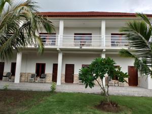 a white house with a balcony and a palm tree at Mama Nings Beach Hotel in Sekongkang