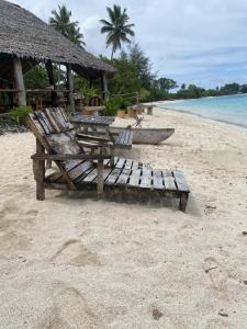 a wooden bench sitting on a beach next to a boat at Port-Olry Beach Bungalows Chez Louis in Port-Olry