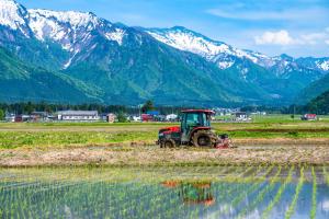 un tractor en un campo con montañas en el fondo en Sakadojo, en Minami Uonuma