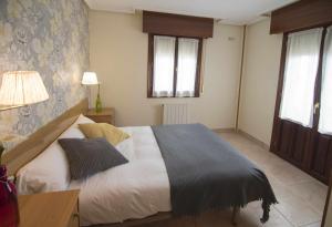 a bedroom with a bed and a table and two windows at Apartamentos Mugarri in Poveña