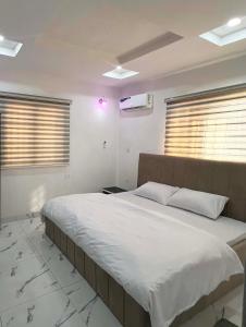 una camera da letto con un grande letto con lenzuola bianche e finestre di Signature Residence a Calabar