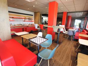 un restaurant avec des banquettes rouges, des tables et des chaises dans l'établissement ibis Aurillac, à Aurillac