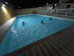 two people swimming in a swimming pool at night at Casa de Praia Martins De Sá Condomínio Caraguatatuba in Caraguatatuba
