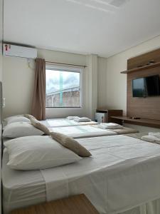 a row of white beds in a room with a window at Hotel Carvalho in Ibiapina