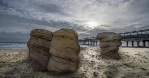 two large rocks sitting on a beach near a pier at Your Oasis - Spacious Family House, Close to Beach, Shops, and Restaurants -Free Parking and Garden, Your Perfect Getaway in Bournemouth