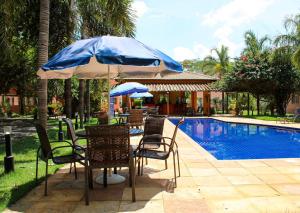 een tafel en stoelen met een parasol naast een zwembad bij Vila Mantilla Pousada in Três Marias