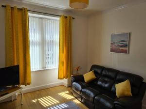 a living room with a black leather couch and yellow curtains at Cosy home in Stornoway