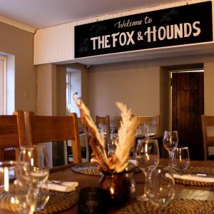 Fox And Hounds Llancarfan في باري: طاولة فيها كاسات و لوحة مكتوب عليها ثعلب و كلاب صيد