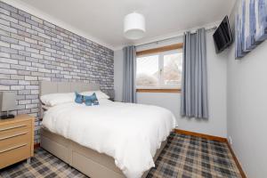 a bedroom with a white bed and a brick wall at ALTIDO Beautiful 3bed house with Garden and Parking in Pitlochry