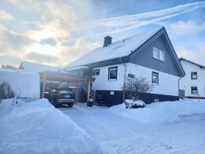 a snow covered house with a car parked in the driveway at Ferienwohnung Haus Schmitt in Winterberg