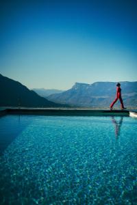 a person walking on the edge of a body of water at Hotel KÜGLERHOF in Tirolo
