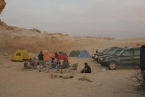 a group of people sitting in the sand next to tents at St.Jadoor Inn in Al Azraq ash Shamālī