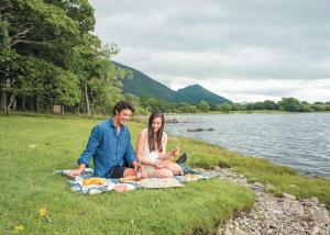 a man and woman sitting on a picnic blanket by the water at Bassenthwaite Lakeside Lodges in Bassenthwaite