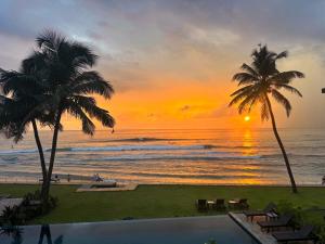 a sunset over the ocean with palm trees and a pool at DORMERO Hotel Sri Lanka Hikkaduwa Beach in Hikkaduwa