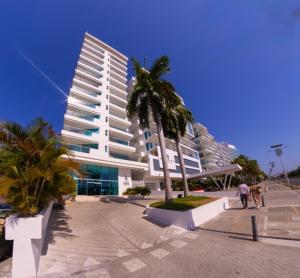 a large white building with palm trees in front of it at Apartmento Edificio Porto Vento in Cartagena de Indias