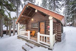une cabane en rondins avec une terrasse couverte dans la neige dans l'établissement Storm Mountain Lodge & Cabins, à Banff