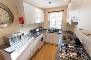 una cocina con armarios blancos y un reloj en la pared en Camstay Abbey Street en Cambridge