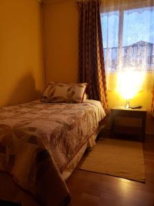 a bedroom with a bed and a window with a lamp at HOSTAL AIRE PATAGON in Coihaique