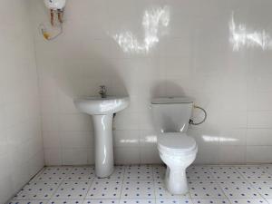 a white bathroom with a toilet and a sink at Izzy Guest House in Brikama