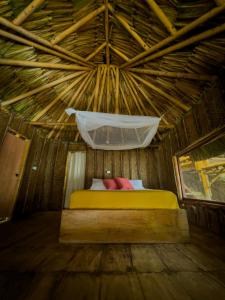 a bed in a thatched room with a mosquito net at Los Achiotes Hostal in Palomino