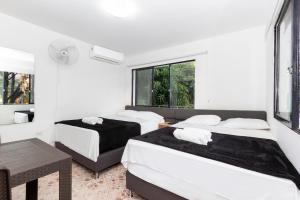 2 camas en una habitación con paredes y ventanas blancas en Hotel De León Estadio en Medellín