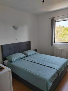 a bedroom with a bed with a blue comforter and a window at Cosy room Arba with private bathroom and sea view in Kampor