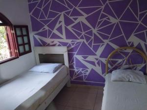 two beds in a room with a purple wall at Guarus house plaza shopping in Campos dos Goytacazes