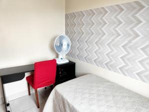 a bedroom with a bed and a red chair and a fan at Condomínio Capim Santo in Goiânia