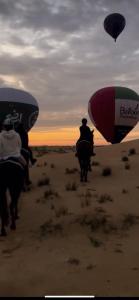 a group of people riding horses in the desert with hot air balloons at Dubaicanam Camp in Dubai