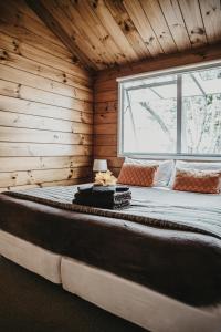 Cama grande en habitación de madera con ventana en Tatahi Cove Back Packer en Hahei