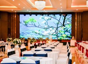 um salão de banquetes com mesas e cadeiras brancas e um grande ecrã em Mường Thanh Grand Dien Bien Phu Hotel em Dien Bien Phu