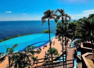 a swimming pool with palm trees and a beach at Studio de Luxo com vista deslumbrante para o Rio in Manaus