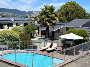 a pool with two chairs and an umbrella next to a house at Arcadia Motel in Nelson